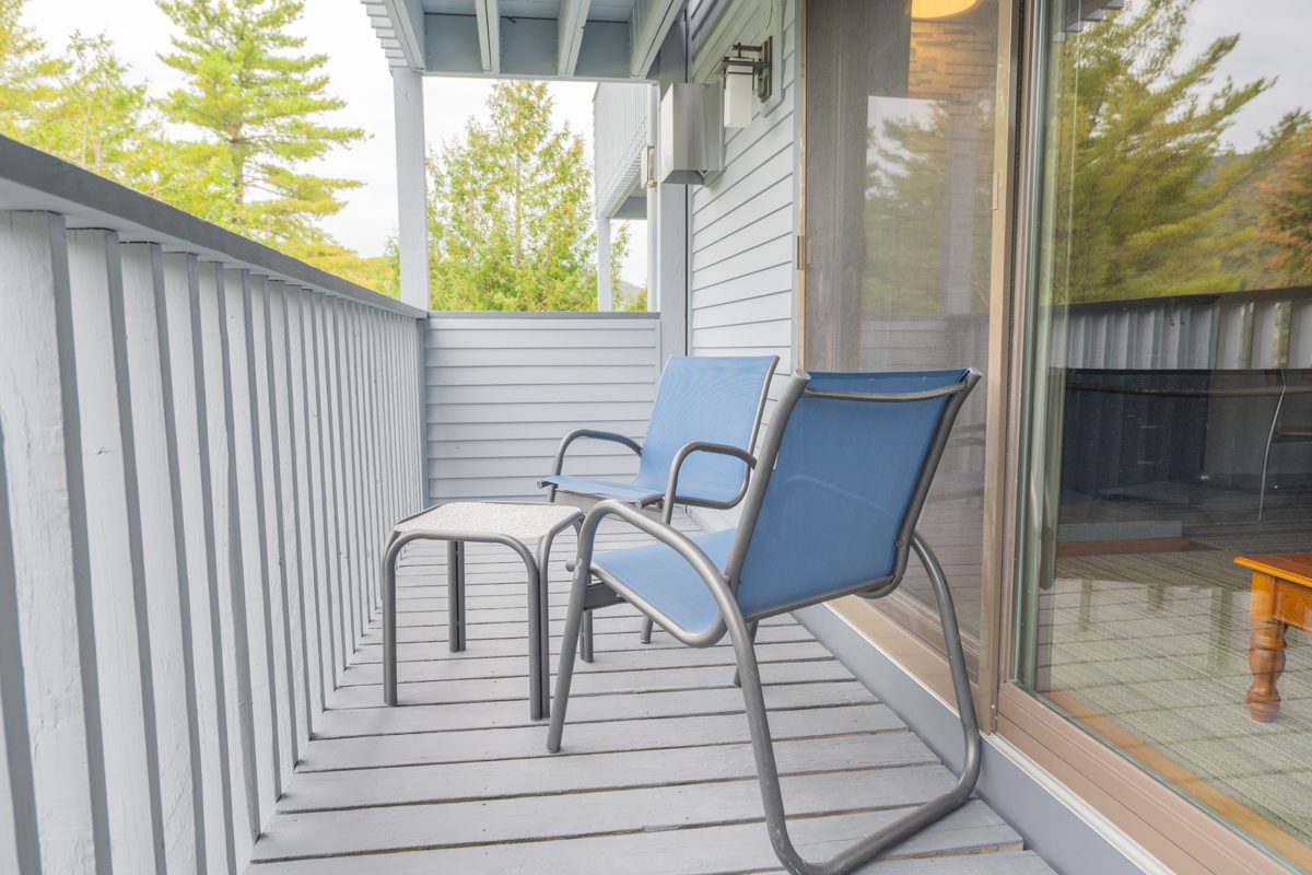 Private balcony at Ski Stash Smuggs with two blue chairs and a side table facing the trees